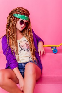 Pretty girl with dreadlocks and green do-rag sitting near the rose skateboard